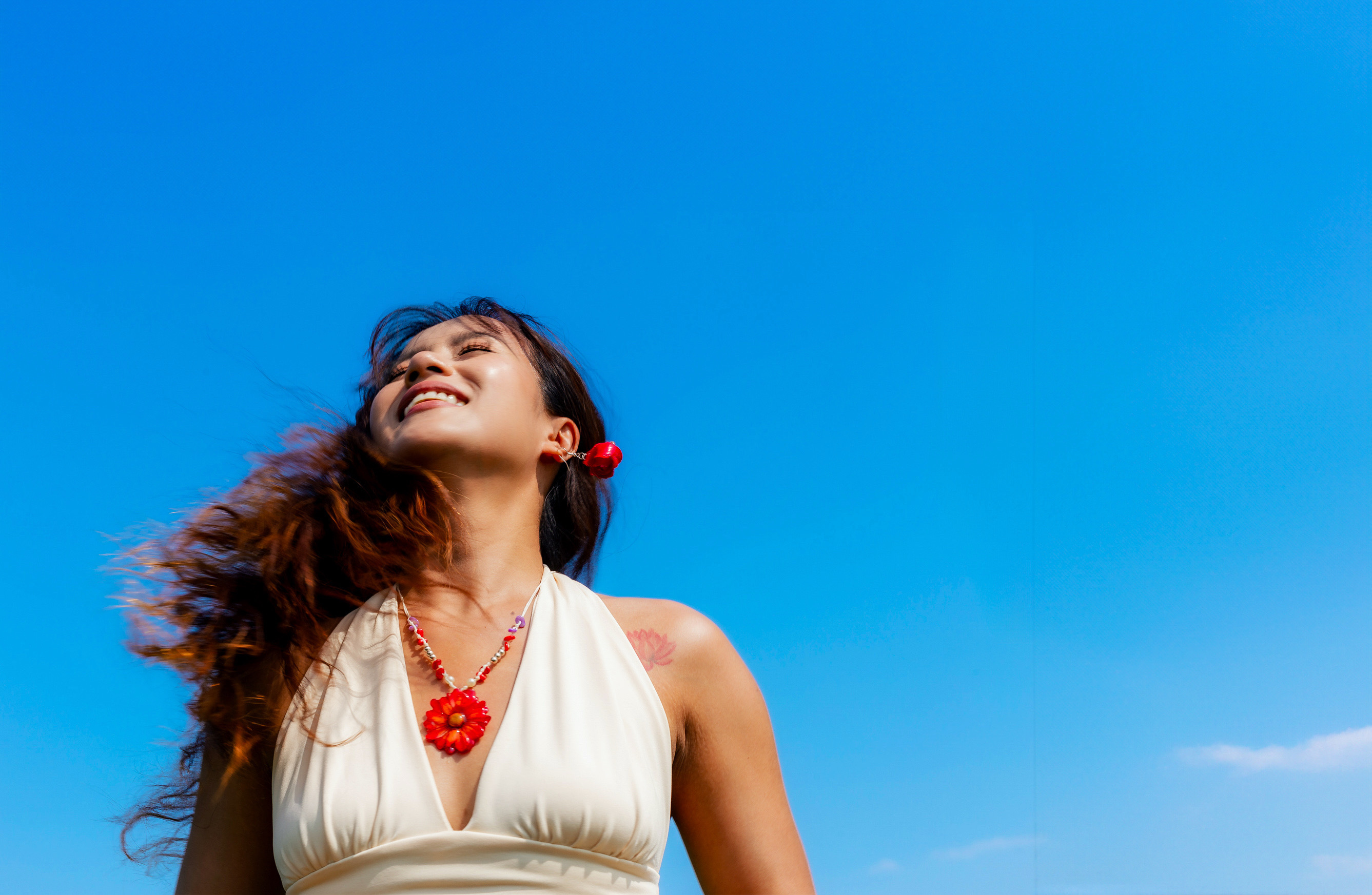 Model wearing red flower jewelry beneath a blue sky